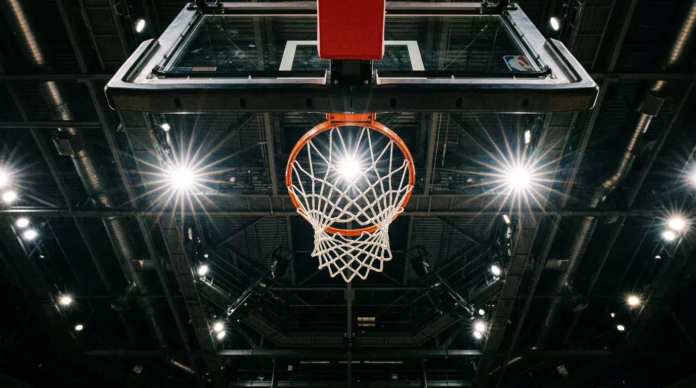 Basketball hoop and backboard seen from below against arena ceiling lights